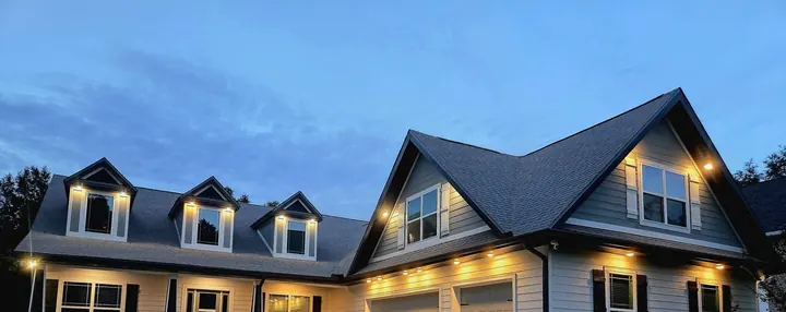 Two-story home with three lit dormers and soffit lighting at dusk