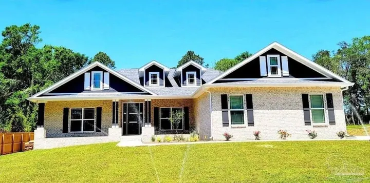 White brick farmhouse-style home with three dormers and black shutters on a green lawn