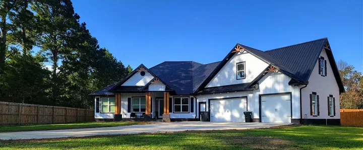 White modern farmhouse with a black metal roof, cedar porch posts and a two-car garage