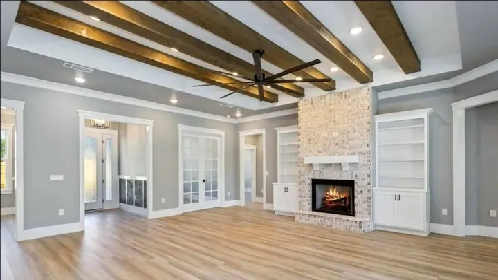 Living room with a whitewashed brick fireplace, built-in shelves, wood beams and French doors