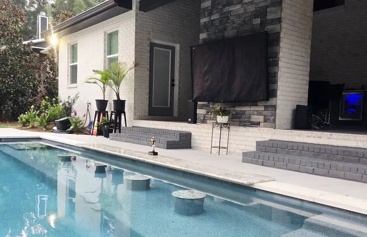 Long pool with a tanning ledge next to a stone outdoor fireplace wall
