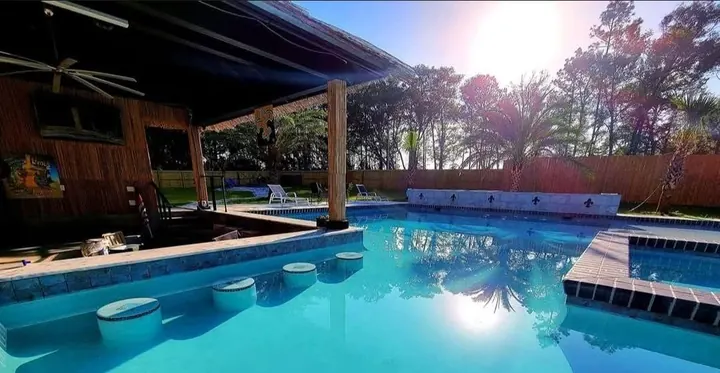 Covered outdoor bar beside a sunlit pool with in-water bar stools