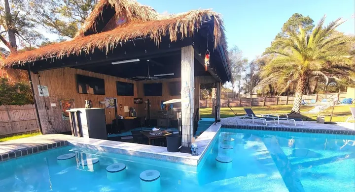 Blue pool with a thatched tiki bar and swim-up stools under palm trees